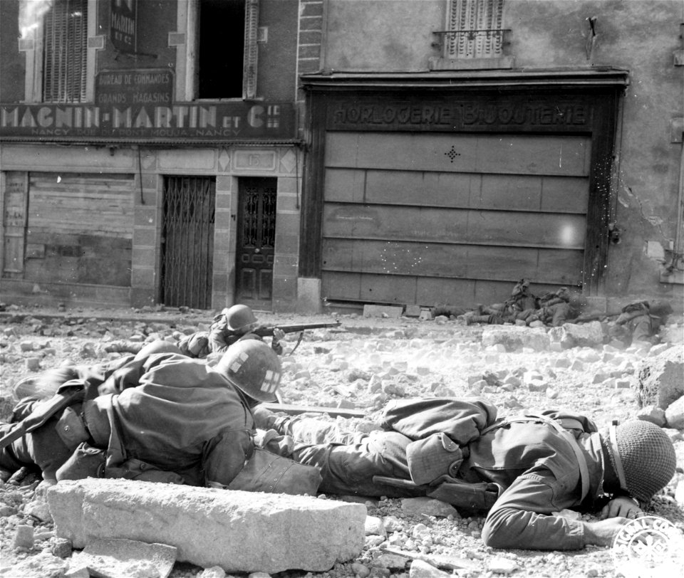 SC 195547 - Capt. Harold L. Render, of El Paso, Ill., lies wounded in foreground, hit by Nazi machine gun slug from across Moselle River while moving through French town of Madiers.