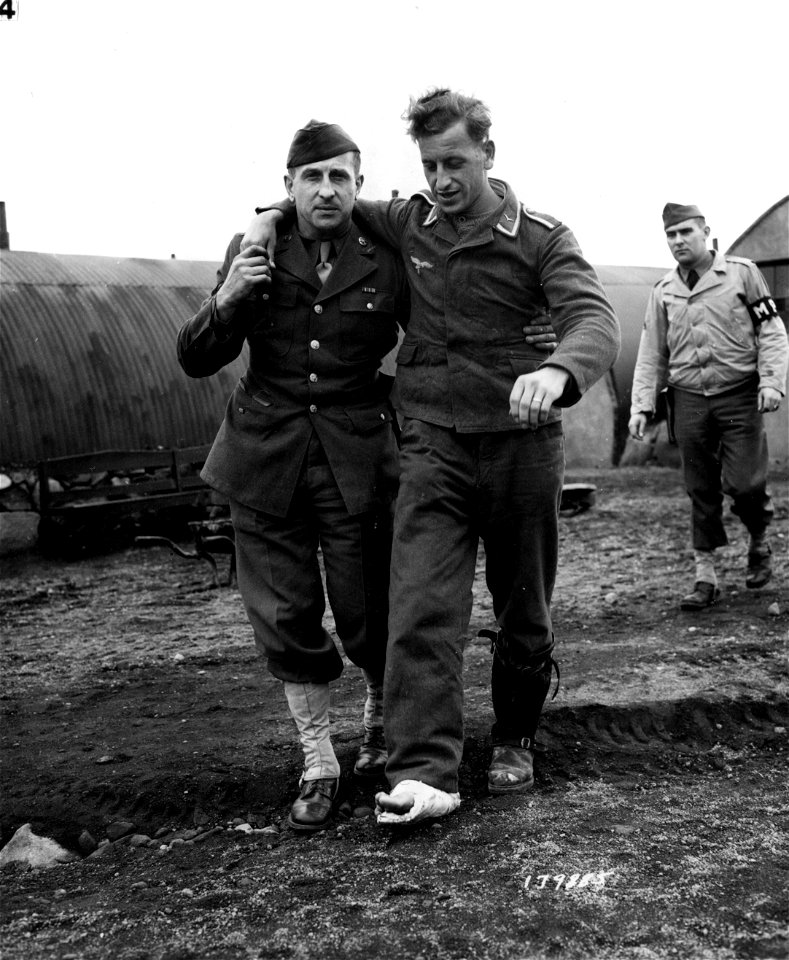 SC 179885 - After interrogation by members of the American Prisoner of War Interrogation Personnel, Unteroffizier Karte is assisted back to quarters by T/4 Fuss.