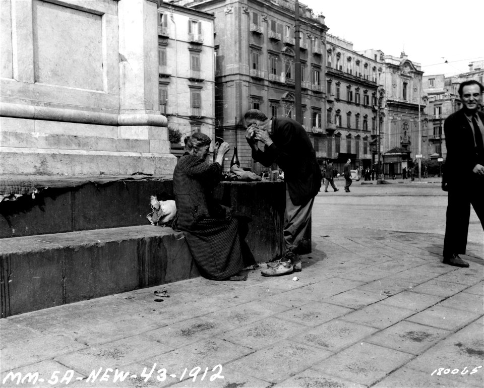 SC 180065 - An elderly Italian man shaves while his wife holds a piece from a broken mirror. Italy. 3 October, 1943.