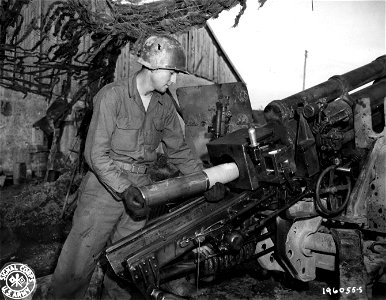 SC 196055-S - A U.S. artilleryman loads a 105mm howitzer with a shell packed with D ration chocolate bars that is to be fired to soldiers of an infantry battalion cut off by the Germans in the Belmont sector, France.