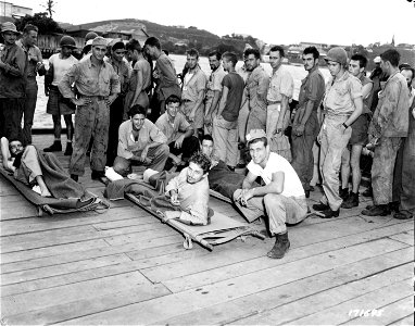 SC 171695 - First Island Command, New Caledonia. Wounded waiting to be transferred to hospitals, munch candy bars on the docks after being unloaded from Higgins Boats following their trip from the Solomon Islands. photo