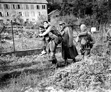 SC 195606 - Japanese-American GIs bring in wounded Jerries in Bruyeres, France. Here, one gets a free ride, probably his last of the war, via the back of one of his comrades. 23 October, 1944. photo