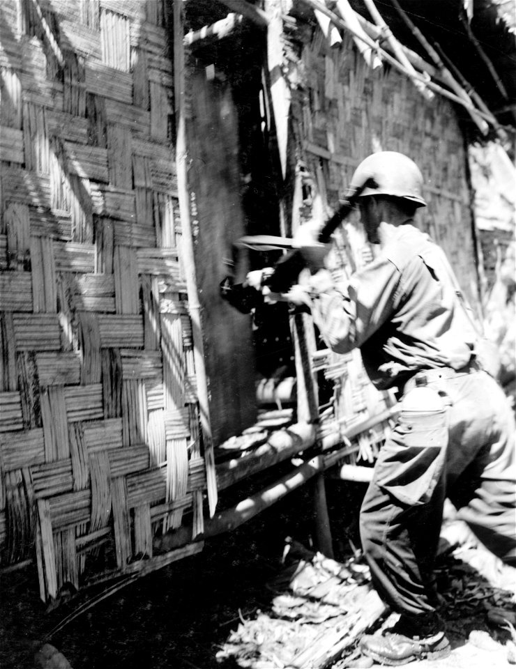 Infantryman knocking door of a hut open with his rifle in native village of [censored], Dutch New Guinea. 1 August, 1944.