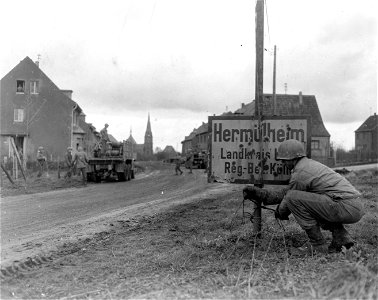 SC 335256 - A wireman of the 8th Division, 1st U.S. Army, ties communication wire to a signpost the edge of the newly taken town of Hermulheim, Germany. 7 March, 1945.