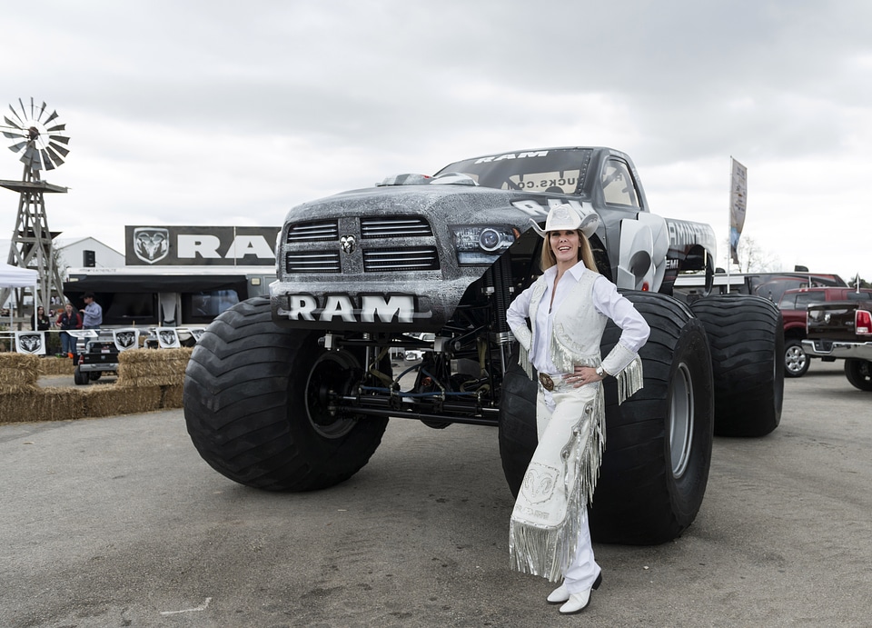 Cowgirl dressed in white standing next to monster truck in Texas