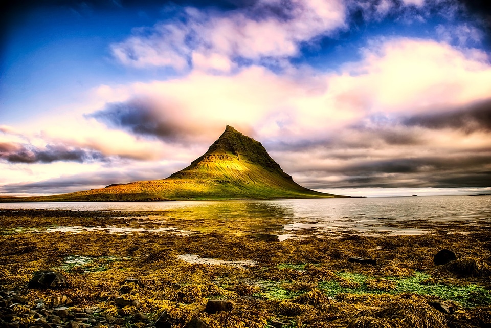 Mountain out of the ocean with clouds over top in Iceland