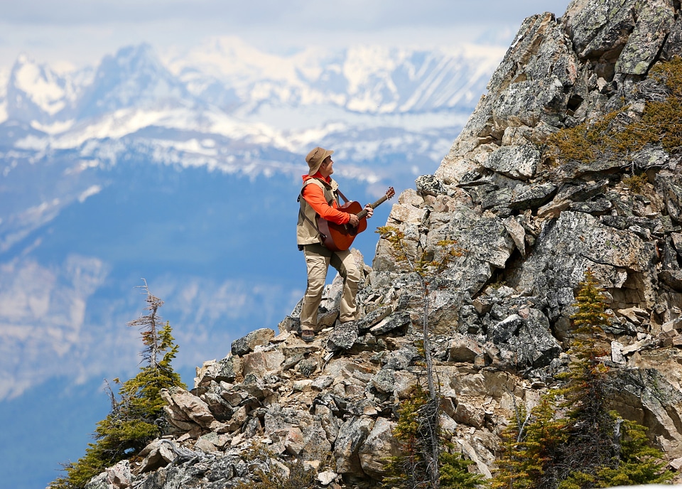 Man Climbing Rocky Mountain while playing Guitar