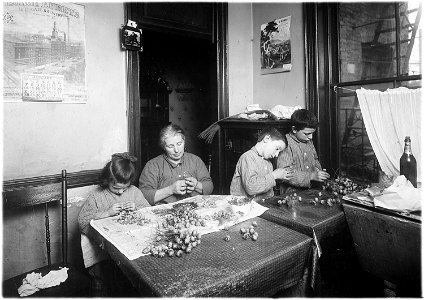 Basso family, making roses in dirty poorly lighted kitchen. Pauline, 6 years old, works after school. Peter, 8, works... - NARA - 523515 photo