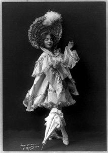 Model posed in ornate costumes- in white, ruffled satin with large plumed hat and parasol LCCN2004678789