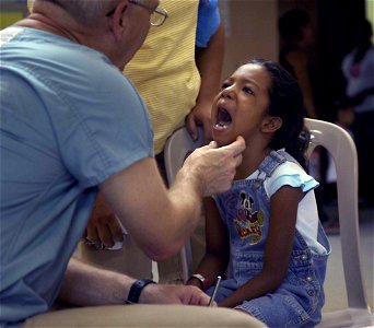 US Navy 090706-F-7923S-039 Cmdr. Matt Herzberg, a dentist embarked aboard the Military Sealift Command hospital ship USNS Comfort (T-AH 20), screens a young Nicaraguan girl to see how his team can help her photo