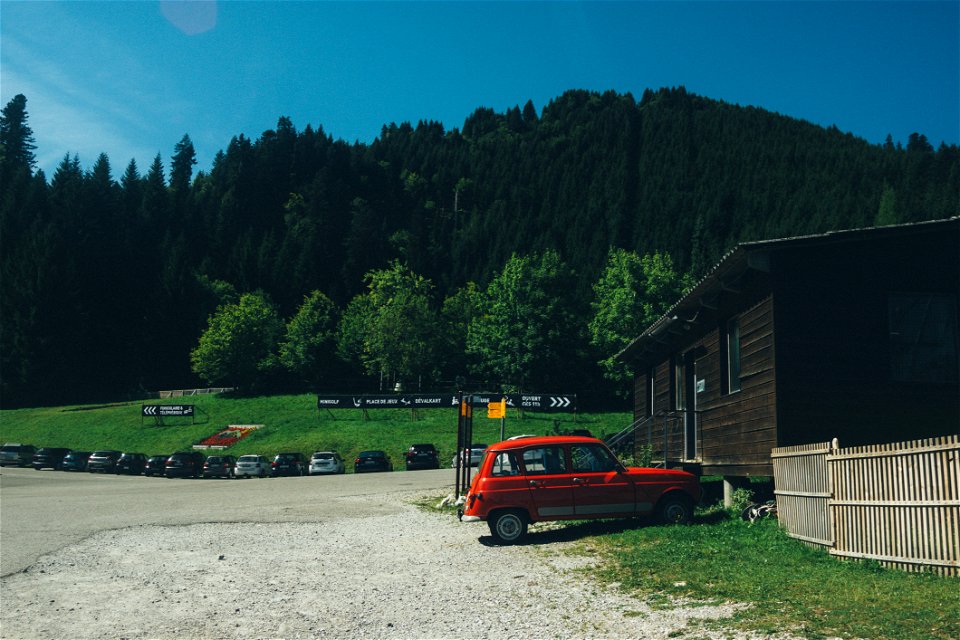 Red 5-door Hatchback Near The Brown Wooden House In Daytime