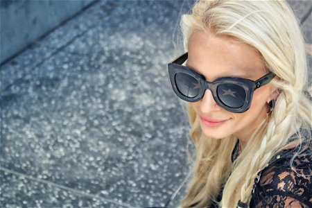 Woman Wearing Black Framed Wayfarer Style Sunglasses And Black Floral Top Near Gray Concrete Pavement