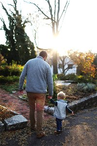 Man Holding Hands With Baby While Walking Through Pathway Facing Sunlight photo