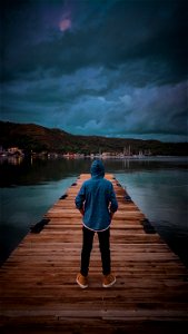 Man Wearing Blue Hoodie Standing On Wooden Dock photo