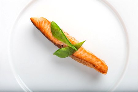 Cooked Fish With Two Green Leaf On Round White Ceramic Plate photo