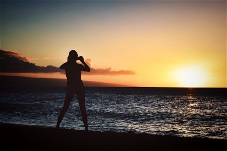 Silhouette Of Woman Holding Camera Near Seashore During Golden Hour photo