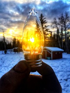 Person Holding Led Bulb In Front Of Sunrise Photo photo