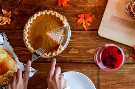 Person Holding Knife And Fork Cutting Slice Of Pie On Brown Wooden Table photo