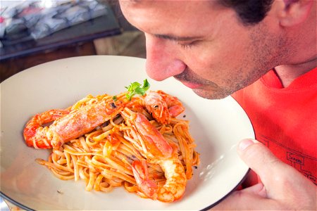 Man Smelling Prawn And Pasta Dish On White Ceramic Plate photo