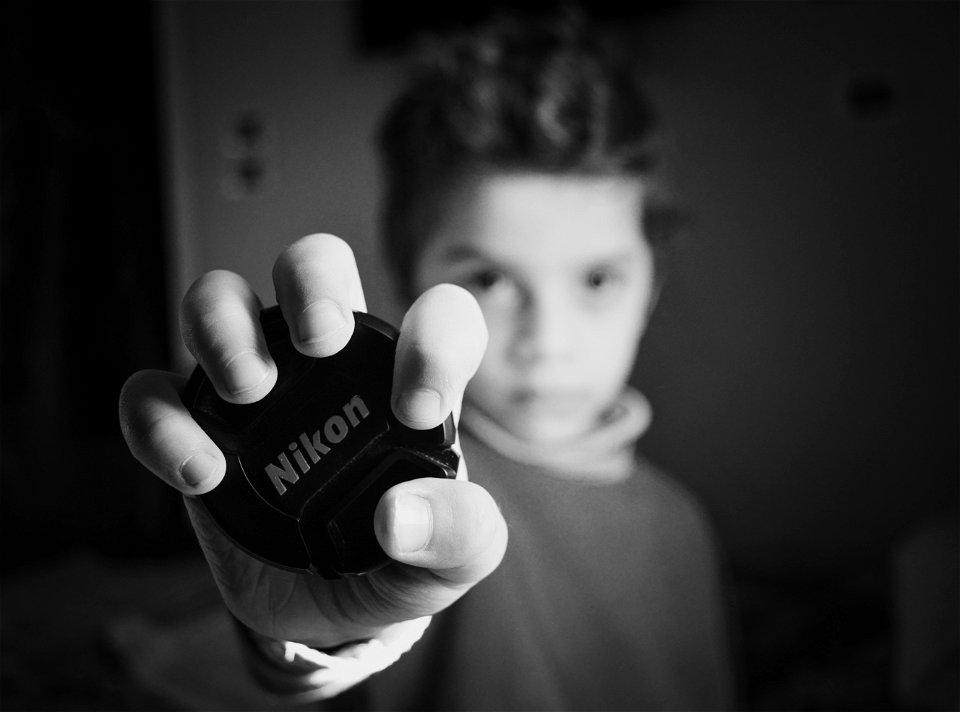 Selective Focus Photography Of Boy Holding Nikon Lens Cover