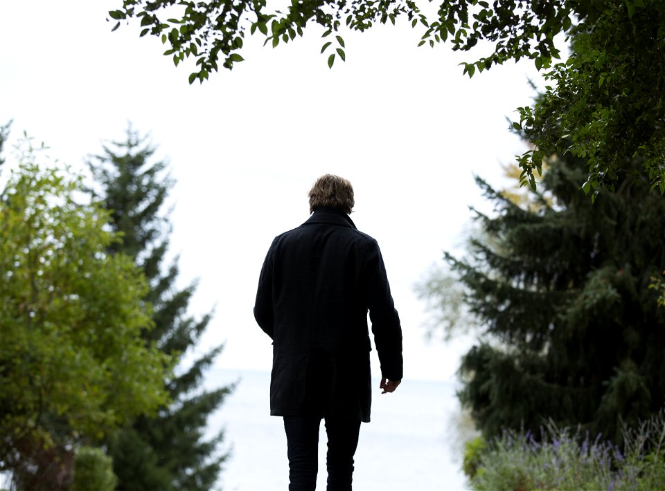 Shallow Focus Photography Of Man Wearing Black Coat And Black Pants Standing Beside Green Trees photo