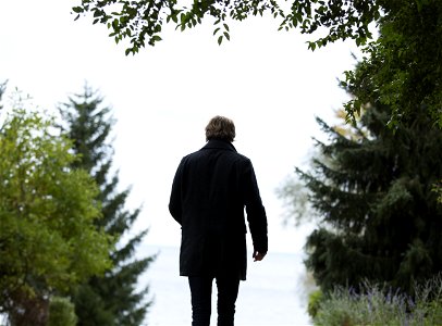 Shallow Focus Photography Of Man Wearing Black Coat And Black Pants Standing Beside Green Trees