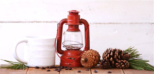 Red Kerosene Lantern Beside White Ceramic Mug On Brown Wooden Table photo