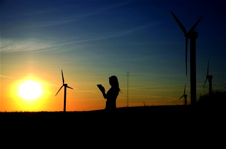 Silhouette Of Woman Holding Book Near Windmills photo