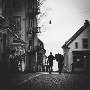 Grayscale Photo Of Man Beside Woman Under Umbrella Walking On Pavement photo