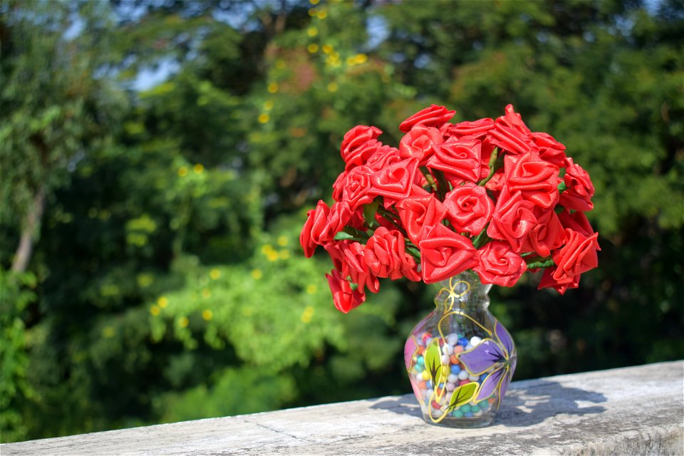 Artificial Roses In Clear Glass Vase On Concrete Surface