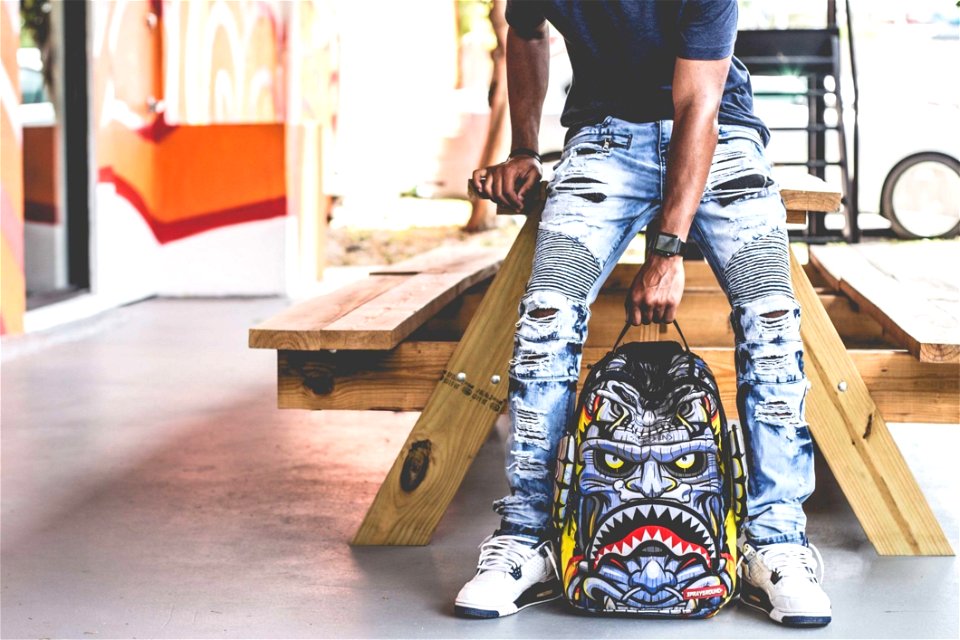 Man Wearing Distressed Denim Pants Holding Multicolored Backpack photo
