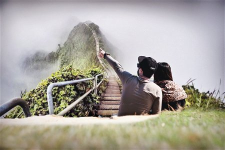 Photography Of Couple Sitting On Green Grass Near Bridge photo