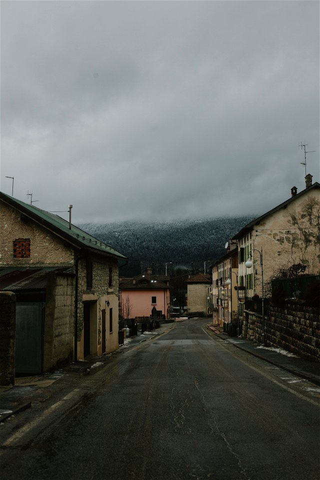 Gray Road Surrounded With Concrete Houses With Background Of Dark Clouds