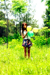 Woman Standing On Grass Field While Holding Three Balloons photo