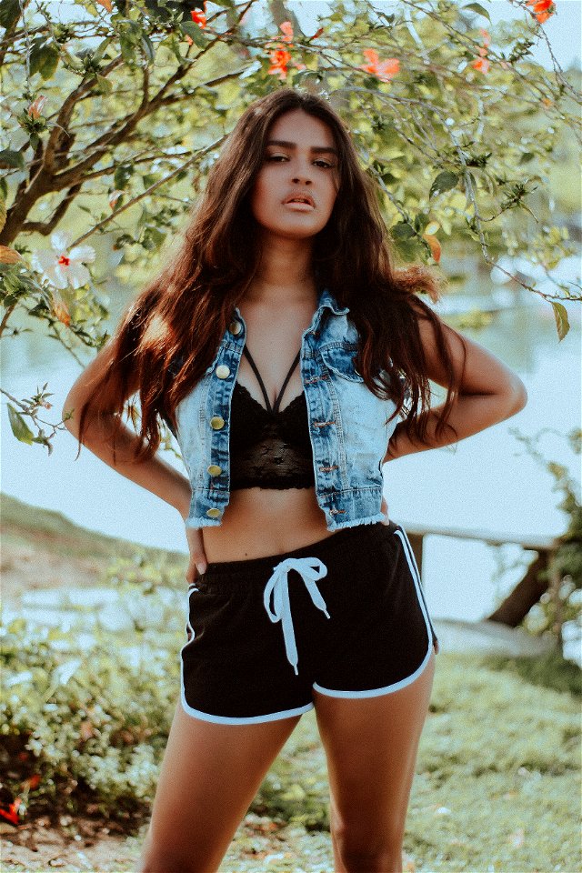Woman In Gray-washed Denim Sleeveless Collared Cropped Top Standing With Background Of Calm Body Of Water