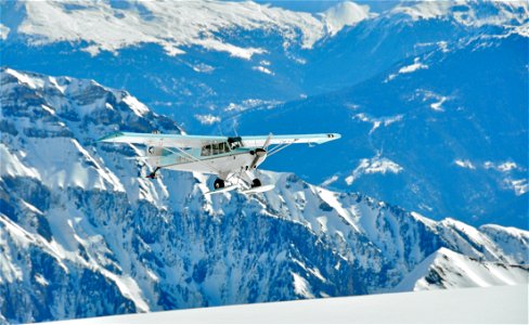 White And Green Monoplane Flying Above Mountains