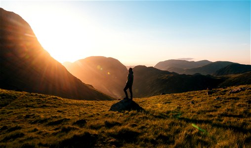 Silhouette Photography Of Person Standing On Green Grass In Front Of Mountains During Golden Hour photo