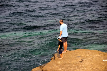 Barefoot Man And Boy Fishing On Rock