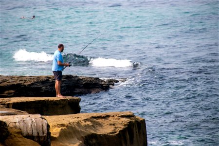 Barefoot Man Fishing On Rocky Shore photo