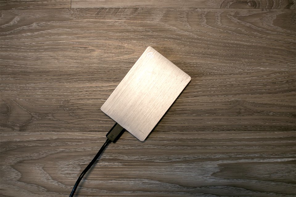 Plugged Silver External Hard Drive On Wooden Surface
