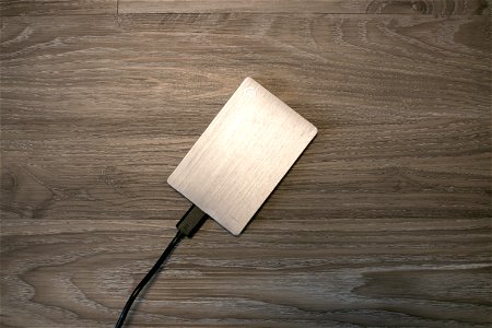 Plugged Silver External Hard Drive On Wooden Surface