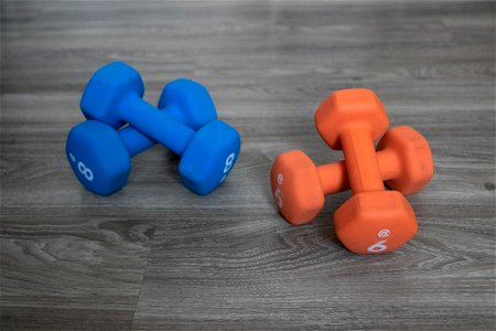 Two Sets Of Brightly Colored Dumbbells On Wooden Surface photo