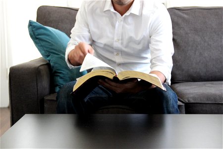 Man on Couch Turning Page of Bible