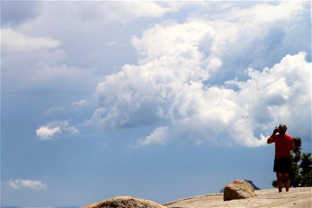 Elderly Man Standing on Rock Under Sky with Puffy Clouds photo