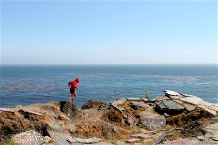 Girl Walking Across Rocks by Ocean photo