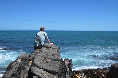 Man Sitting on Rock Looking at Ocean photo
