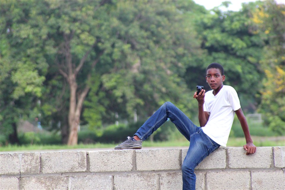 Teen Boy Sitting on Brick Wall with Camera