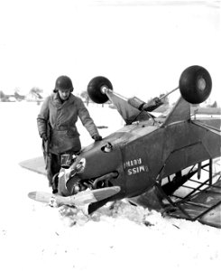 SC 198857 - Pvt. Robert V. Long, Washington, D.C., a member of a signal photographic unit, examines the damaged engine and propellor of a 6th Armored Division liaison plane after it toppled over while making a landing at an air strip in Belgium. photo