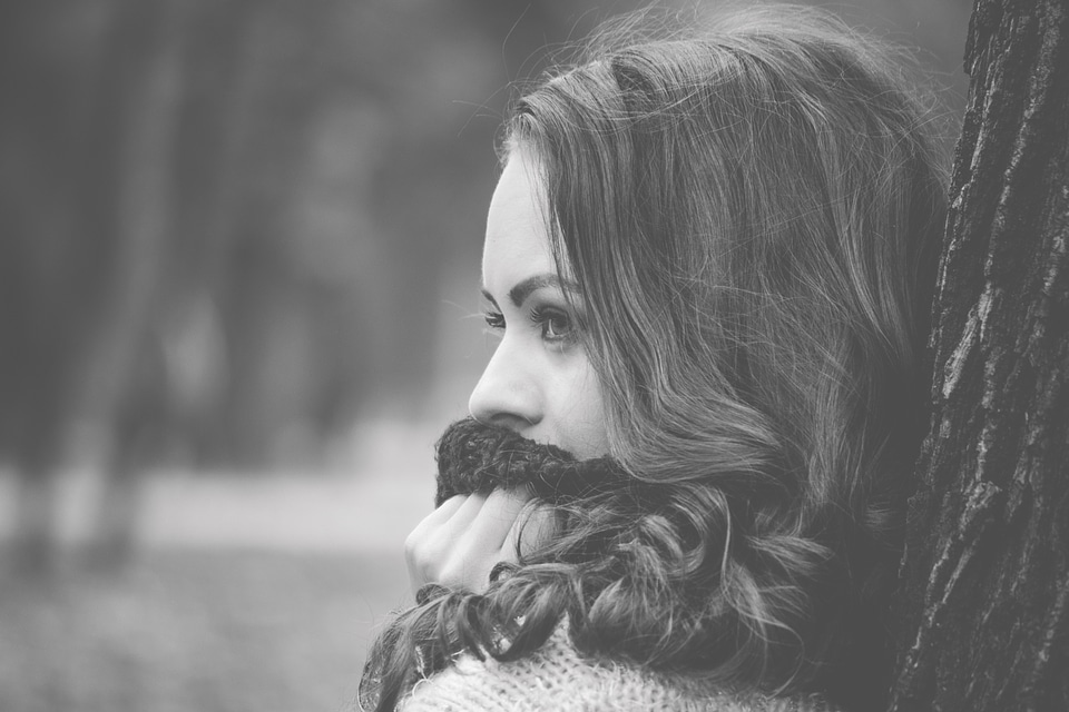 Girl Looking Away with a Scarf on the Mouth and leaning by a Tree
