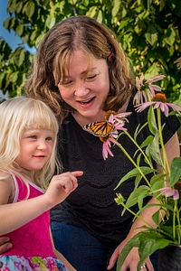 Mother and daughter look at monarch on flower